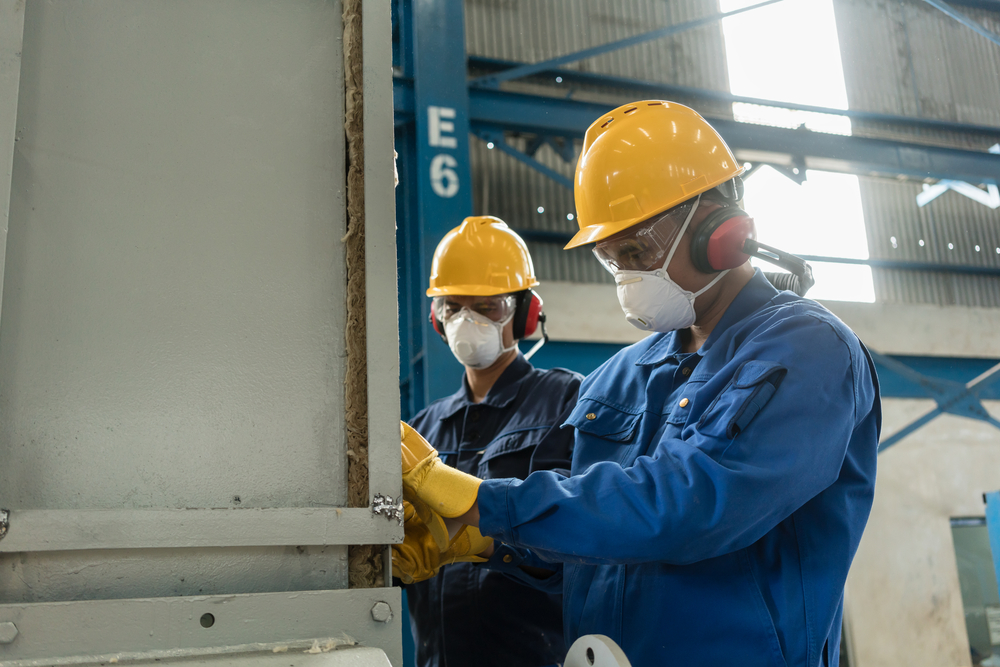 Two blue-collar workers in hardhats and face masks to illustrate workers compensation executive orderswearing protective equipment