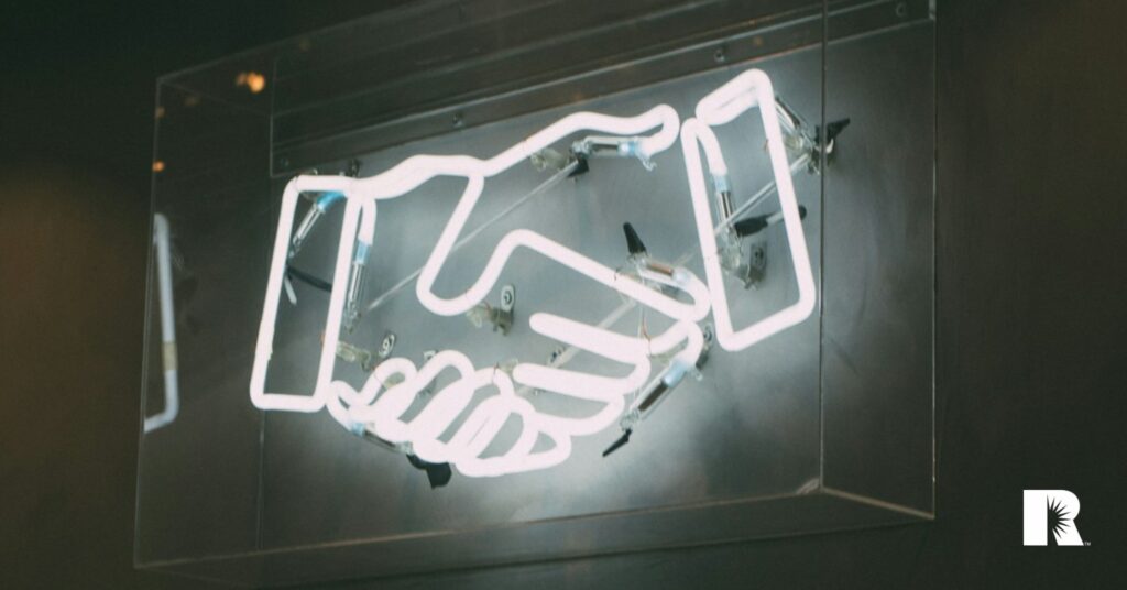 An image of a neon sign of two hands being shaken.